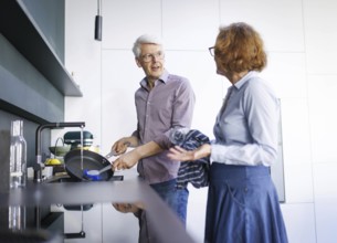 Symbolic photo. An elderly couple stand in the kitchen and do the washing up together. Berlin, 13