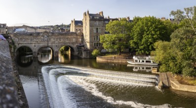 River with waterfall and bridge, surrounded by urban landscape and nature, Bath