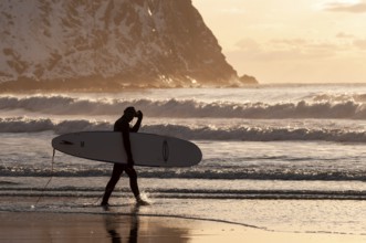 Surfer with surfboard under his arm on the beach of Unnstad, winter surfing, Lofoten Island