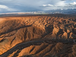 River bed runs through a landscape of eroded hills, badlands at sunset, mountain peaks of the Tian