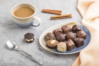 Different chocolate candies and a cup of coffee on a gray concrete background and orange textile.