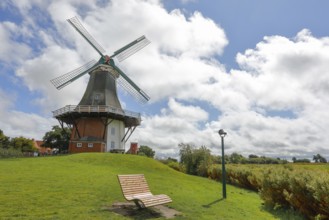 A windmill in front of a dramatic blue sky, surrounded by green meadows with a deckchair,
