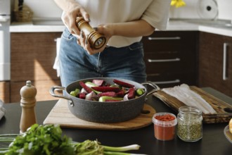 Close-up view of female hands sprinkle pepper from manual spice mill on vegetables in a baking pan