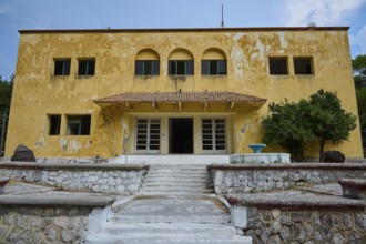 An old yellow dilapidated building with a damaged façade and a staircase in the entrance, Italian