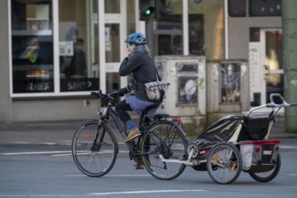 Woman riding a bicycle and child trailer, talking on mobile phone while riding, Bochum, North