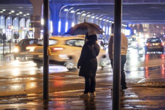 Illuminated subway at the main railway station, pedestrians at a pedestrian crossing, rainy
