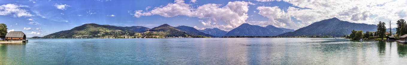 Clear water of a lake with surrounding mountains, on a sunny day with blue sky and white clouds,
