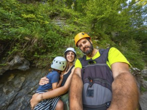 Happy family wearing helmets and backpacks taking a selfie while hiking in vintgar gorge near bled,