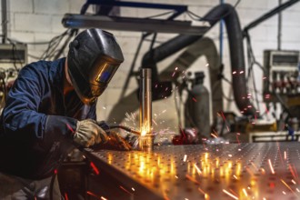 Unrecognizable male welder with protective facial mask and gloves welding a piece of metal in a