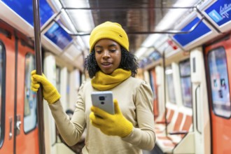 Young black woman dressed in vibrant yellow winter clothes, using her smartphone while standing