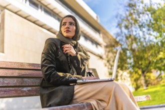 Muslim businesswoman working with laptop outdoors sitting on a bench in a park
