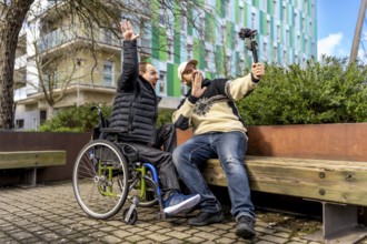 Two cheerful content creators, one in a wheelchair, are recording a video blog in an urban setting,