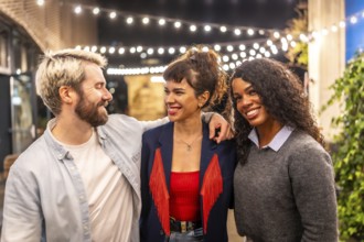 Happy friends embracing and smiling standing in a roof terrace at night celebrating party