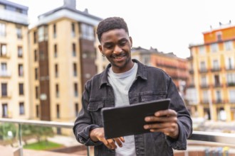 Happy african man touching the screen of a digital tablet and smiling outdoors in the city