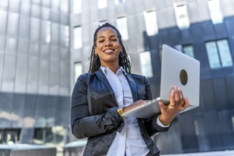 Portrait of a casual latin businesswoman standing with laptop outdoors in the financial district
