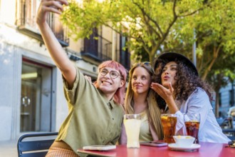 Diverse modern latin and caucasian women flowing kiss while taking selfie in an outdoor terrace