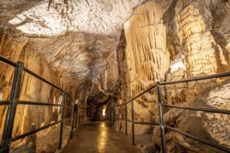 Tourists walking on illuminated pathway, admiring stalactites and stalagmites inside postojna cave,