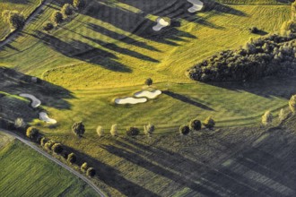 Aerial view from a hot air balloon of a golf course surrounded by trees and long shadows, Wenden,