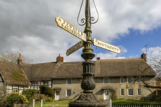 Historic signpost with direction painters, thatched cottages in village of Pewsey, Wiltshire,