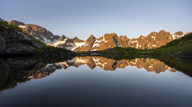 Rocky mountain peaks reflected in a small pond, mountain landscape with alpenglow at sunrise, at