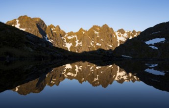 Rocky mountain peaks reflected in a small pond, mountain landscape with alpenglow at sunrise, at