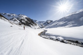 Ski tourer in the snow by a mountain stream in the Funtauna Valley, Sonnenstern, Graubünden Haute