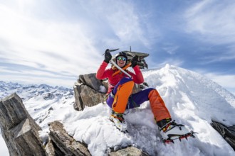 Happy mountaineer with ice axes and crampons on the summit of Piz Grialetsch in winter, Graubünden