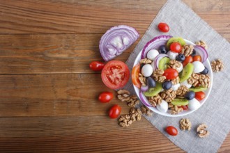 Salad with fresh cherry tomatoes, mozzarella cheese, olives, kiwi, onion and walnuts on brown