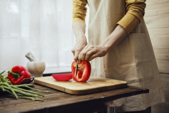 Unrecognizable man slicing red bell pepper with kitchen knife in the kitchen