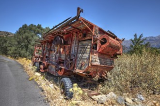 Dilapidated, rusted combine harvester next to the road under blue sky, wrecked vehicle, Crete,