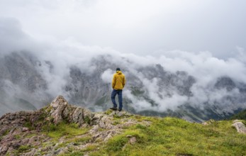 Mountaineer with yellow jacket looking at mountain landscape, cloudy rocky mountain peaks Wolayer