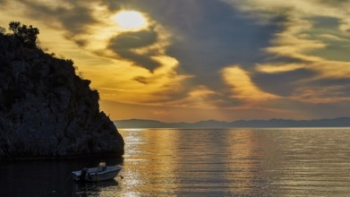 Atmospheric sunrise over the sea with cliffs and a boat, Mani Peninsula, Peloponnese, Greece,