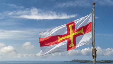 The flag of the Isle of Guernsey, Great Britain, flutters in the wind