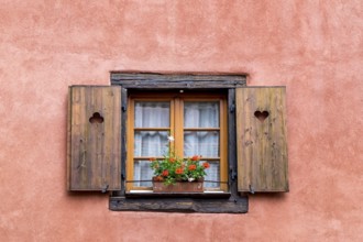 Old window with wooden shutters and flower box, framed by a pink wall, creates a rustic and