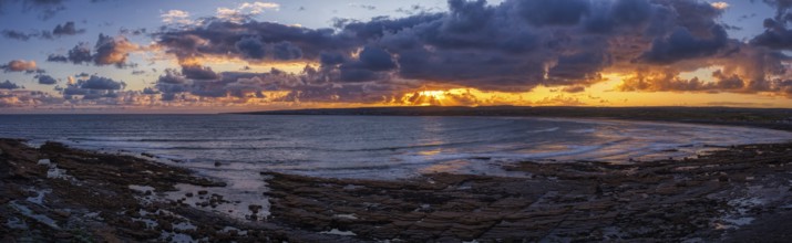 Dramatic sunset over the sea with dark clouds and rugged coastline, Lahinch Beach