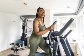 Businesswoman wearing olive green activewear using elliptical cross trainer in hotel fitness center