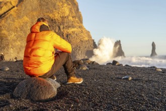 A man sitting on the Reynisfjara Black Sand Beach looking at the beach with a wave