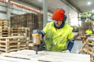 Man manual worker using compressed air gun to arrange pallets to reuse in a recycling plant