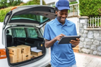 African delivery man using digital tablet standing next to van with packages to deliver