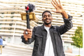 African man vlogger waving at camera while recording video blog in the city