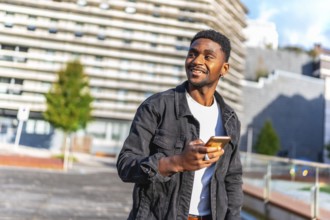 Distracted handsome young african man using mobile app walking along the city