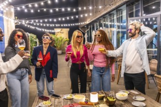 Multi-ethnic young group of people drinking standing at bar terrace at night