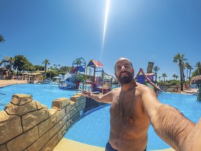 Bearded man enjoying a fun summer vacation at a water park, capturing joyful moments with a selfie