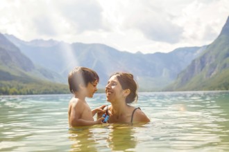 Mother and son enjoying summer holidays, playing in the refreshing water of lake bohinj, surrounded