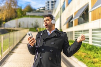 Happy adult man in elegant clothes enjoying listening to music, singing and dancing at city in