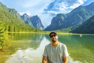 Tourist relaxing by lake dobbiaco, surrounded by the stunning peaks of the dolomites on a beautiful