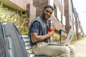 African businessman working with laptop while drinking from reusable bottle sitting on a street