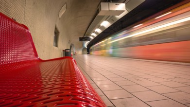 Modern underground railway track bed with red bench and passing train at high speed