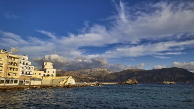 Morning light, coastal town with buildings by the sea and mountains in the background, Pigadia,
