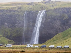 Tourist groups at waterfall Seljalandsfoss on a rainy day, queue at the path behind the waterfall,